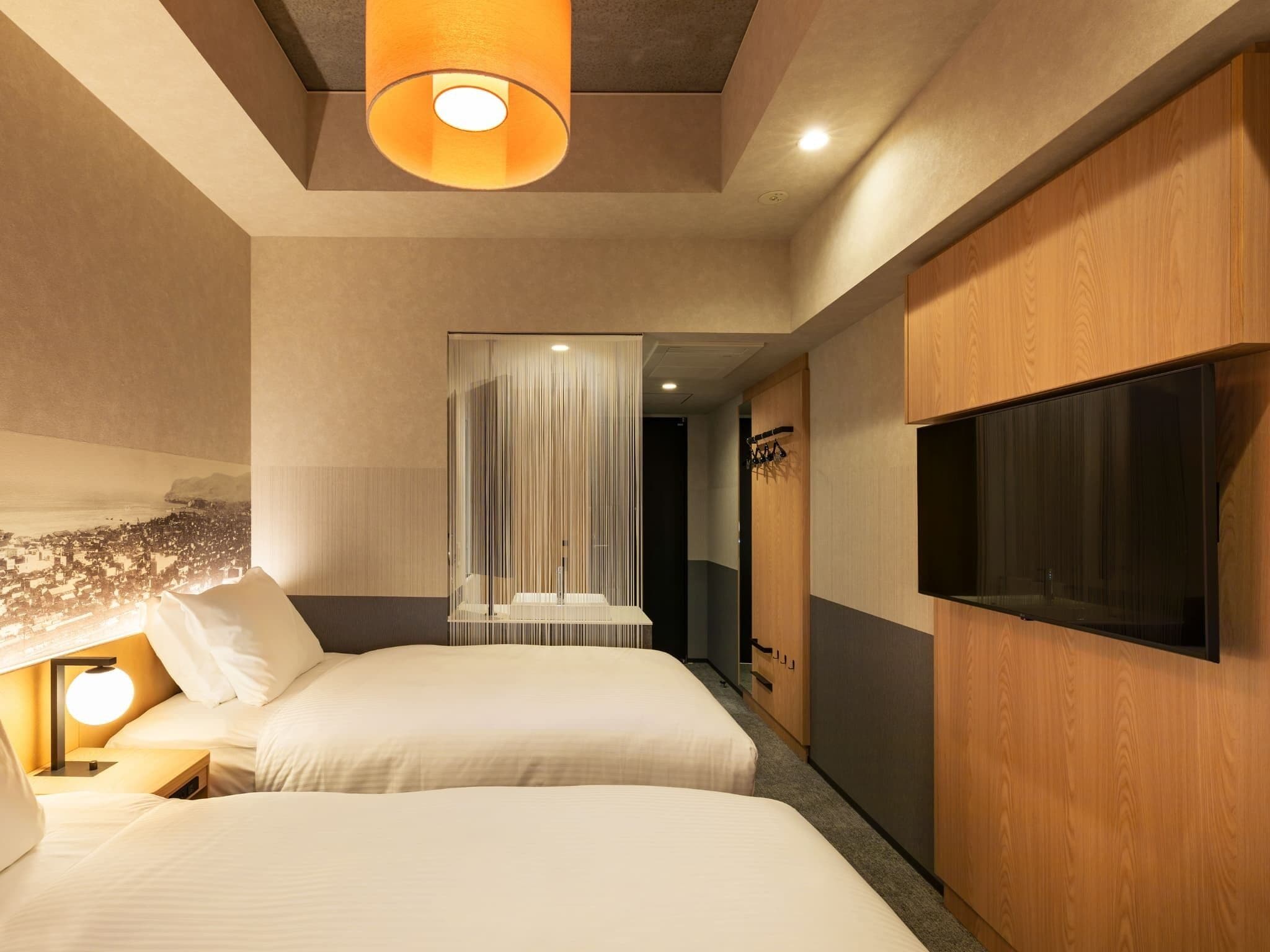 Habitación de hotel con dos camas, un televisor montado en la pared, una lámpara en el techo y un armario de madera.