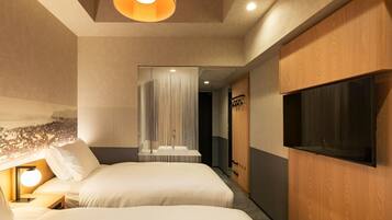 Habitación de hotel con dos camas, un televisor montado en la pared, una lámpara en el techo y un armario de madera.