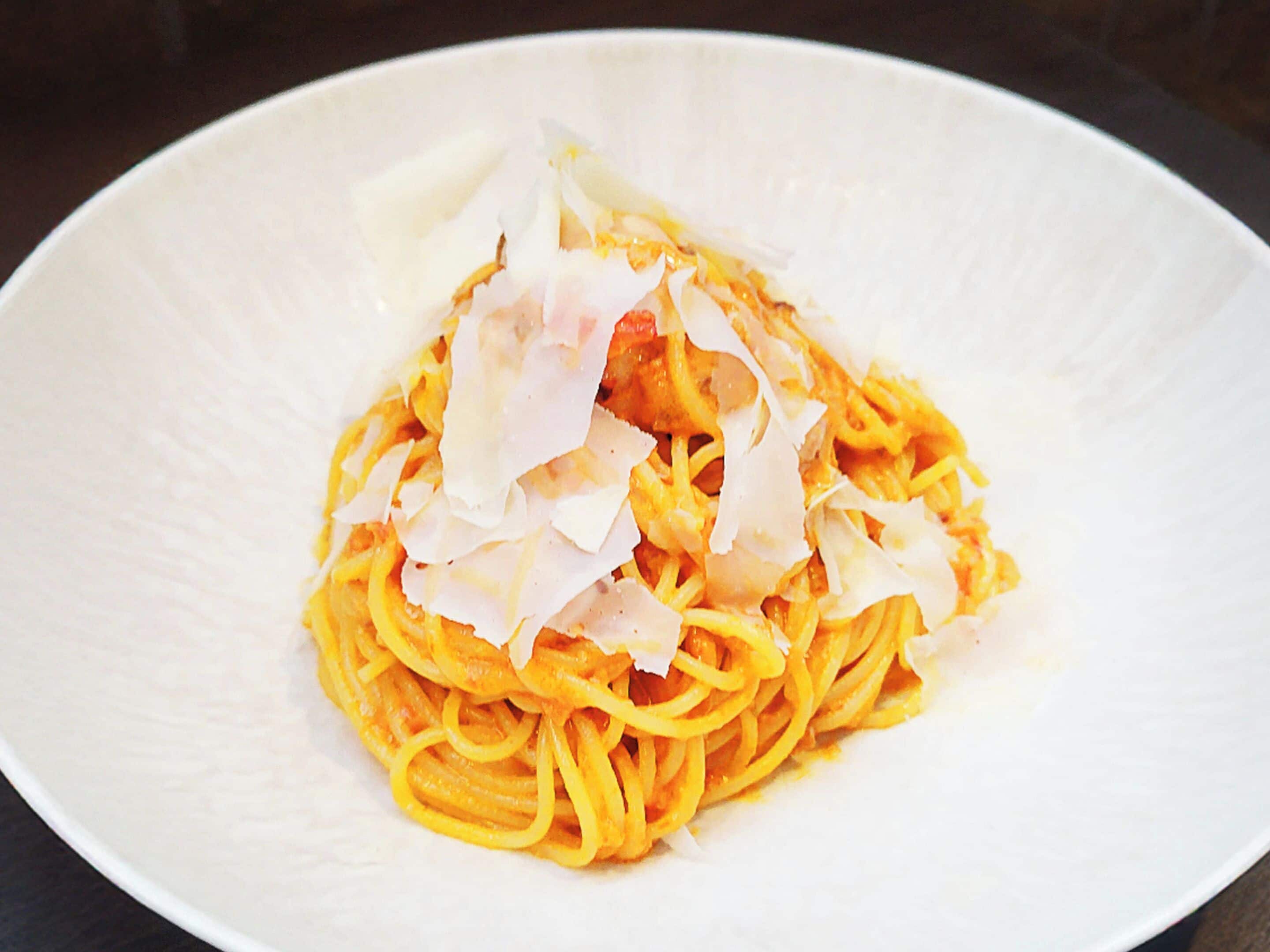 A plate of spaghetti with a creamy sauce and shaved Parmesan cheese.
