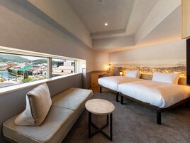 Una habitación de hotel con una cama, un sofá, una mesita y vistas a un paisaje urbano a través de un ventanal grande.