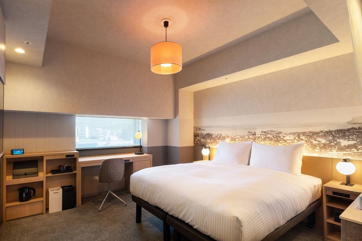A modern hotel room with a large bed, a desk, and a chair.
