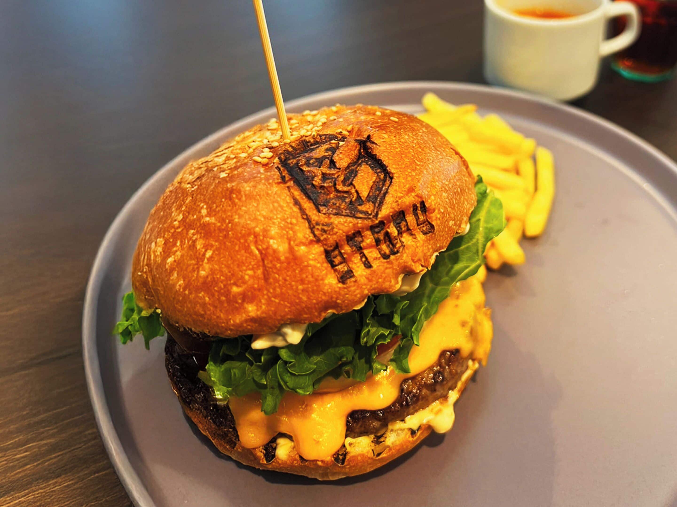 Een hamburger met geroosterd broodje, sla, kaas en een patat, geserveerd op een bord met friet.