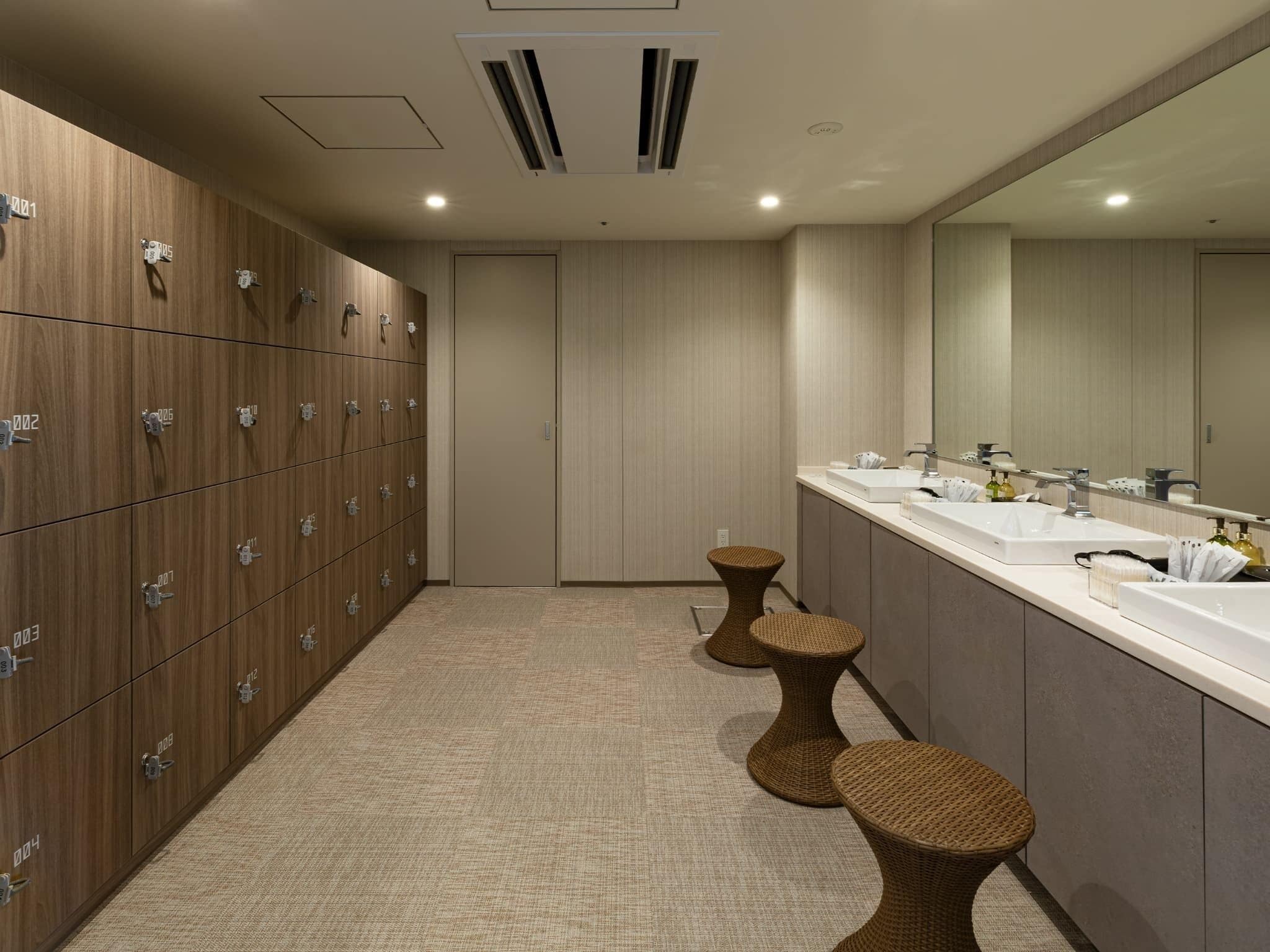 A modern bathroom with wooden lockers, a large mirror, and two wicker stools.