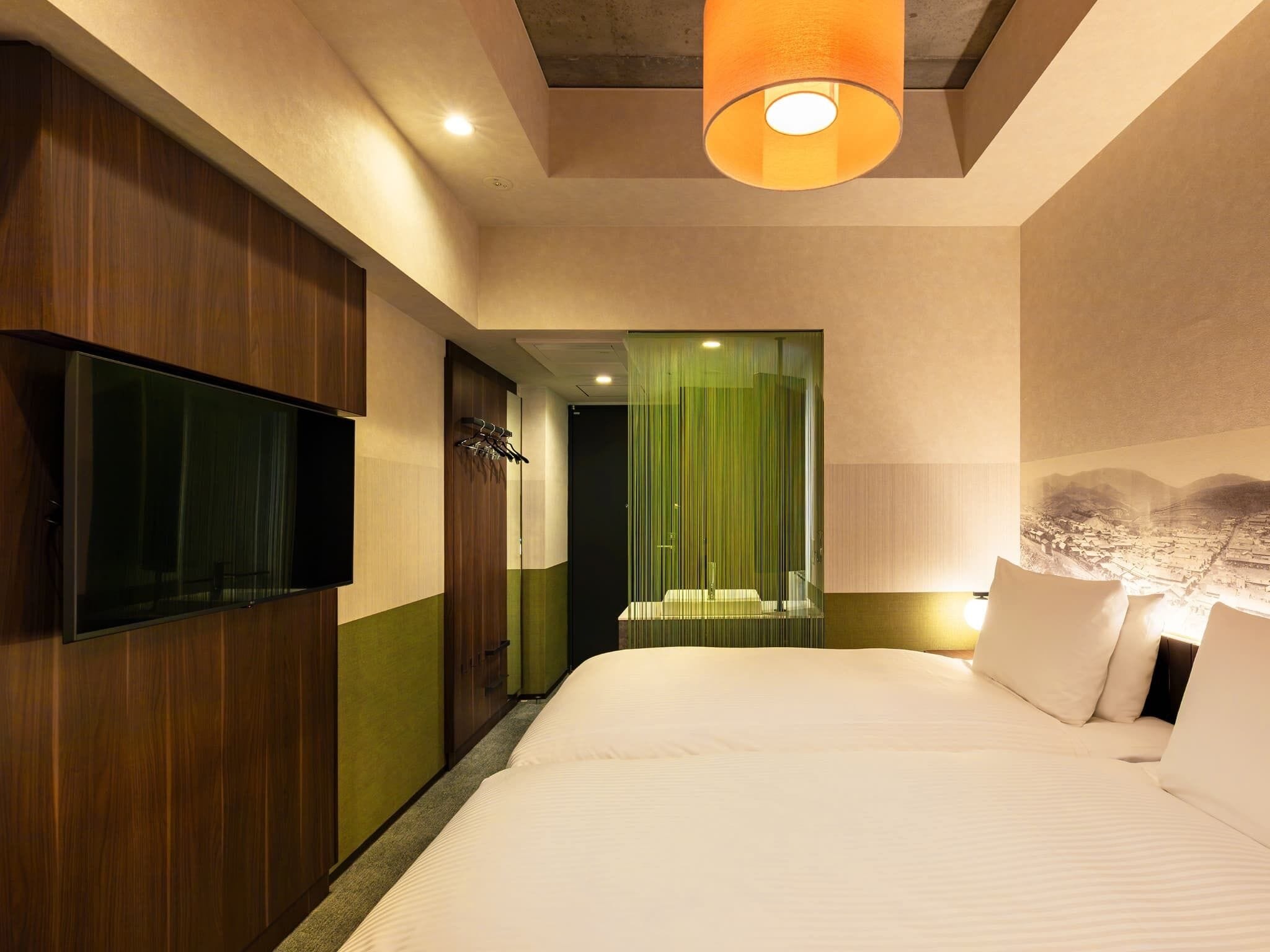 A modern hotel room with a large bed, a flat-screen TV, and a green-striped shower curtain.