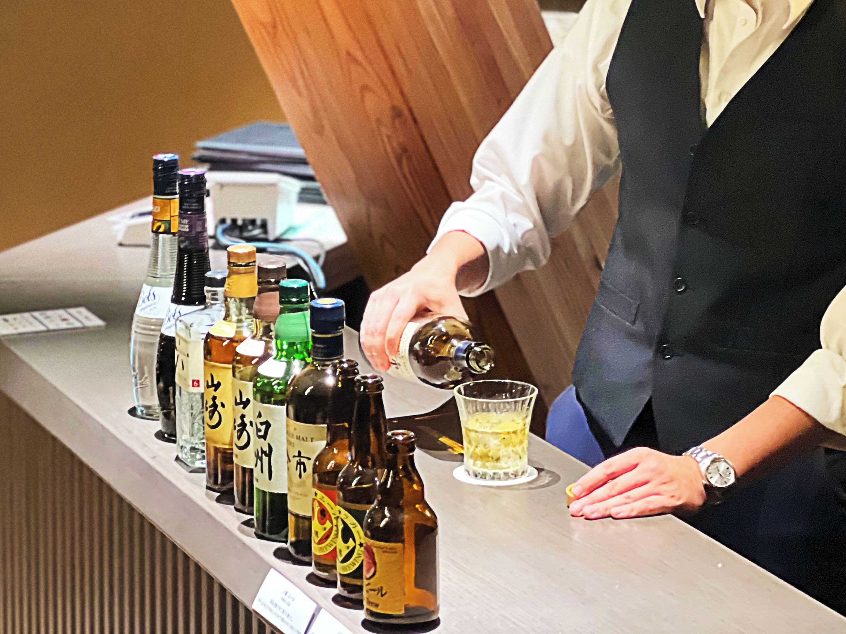 Eine Bar mit verschiedenen Spirituosenflaschen und einer Person, die ein Getränk einschenkt.