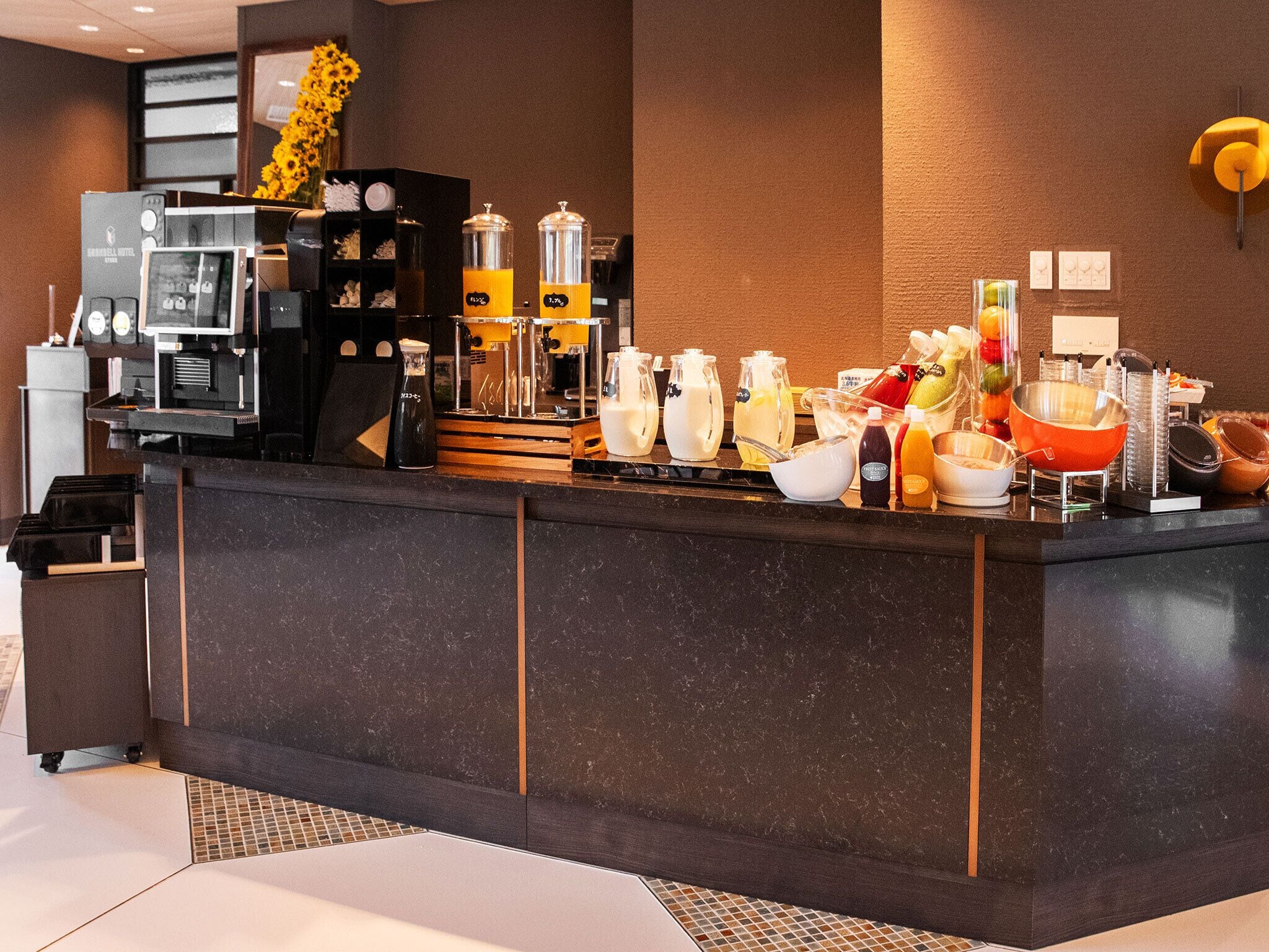 A hotel reception area with a coffee machine, dispensers, and a variety of food and drink containers.