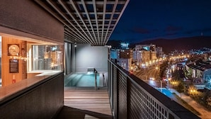 Een balkon met uitzicht op een stadsbeeld 's nachts, met een zwembad en een houten terras.