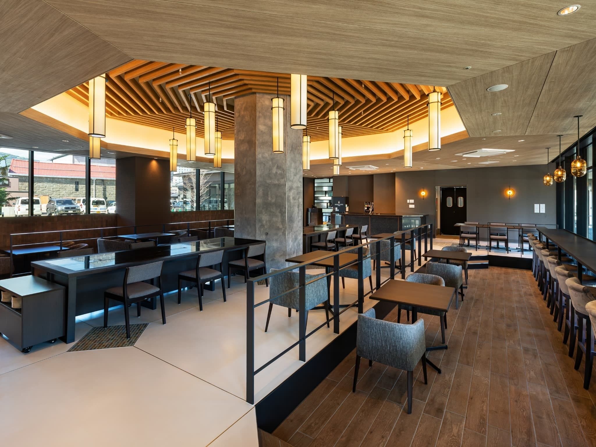 A modern restaurant with a mix of booth and table seating, a central bar area, and a view of the outside through large windows.