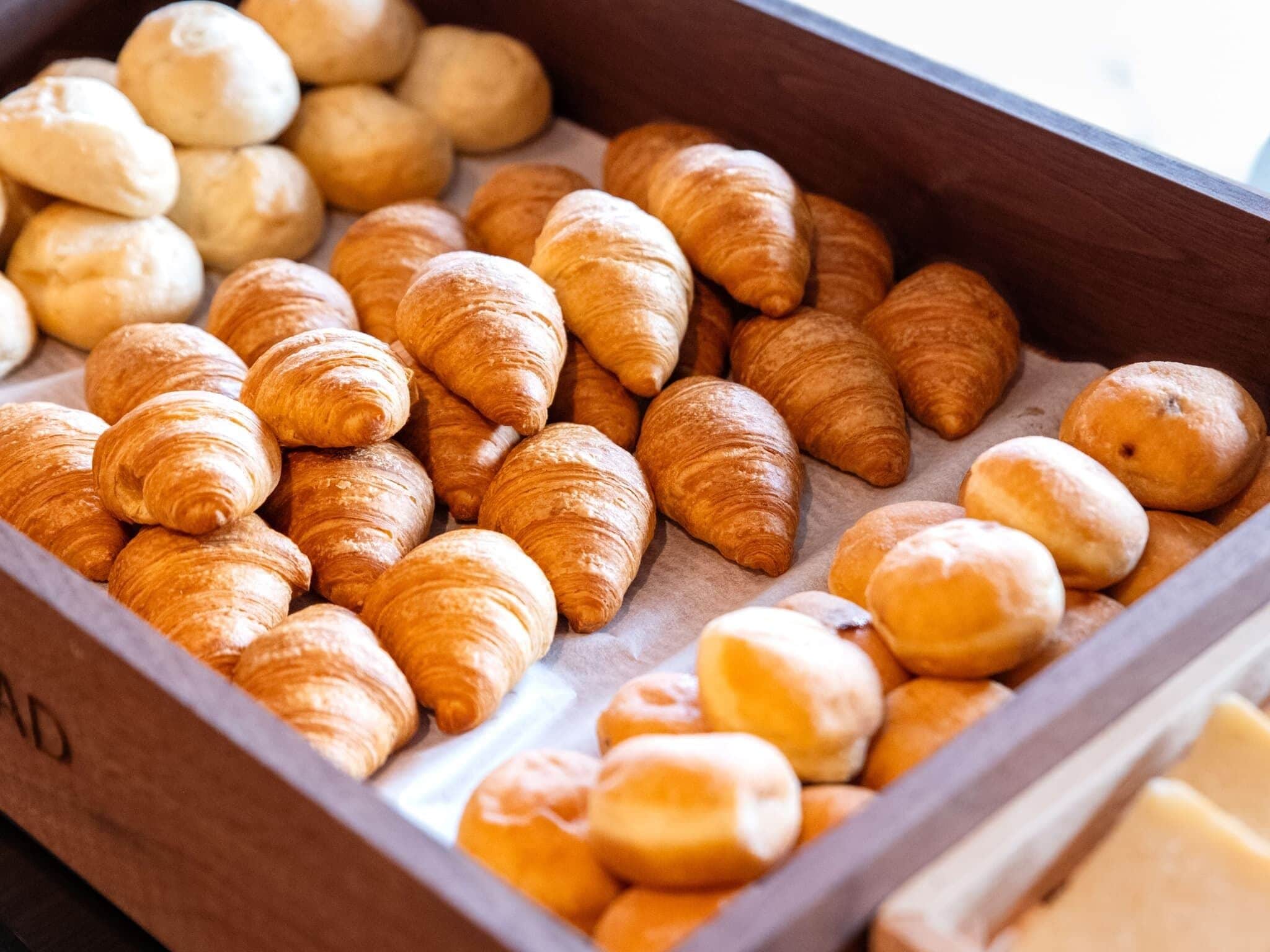 A wooden box filled with various types of bread, including croissants and round loaves.