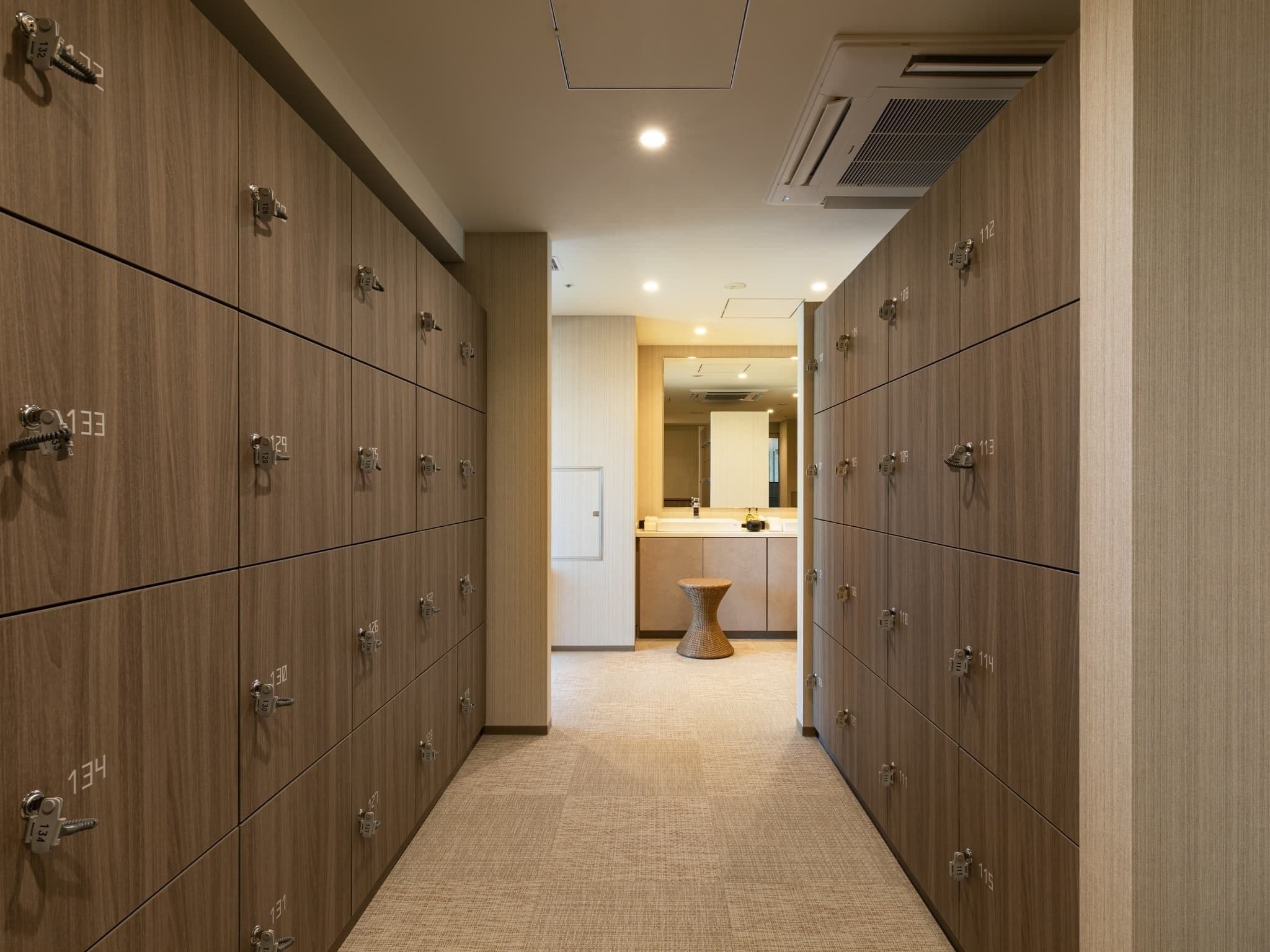 A hotel corridor with lockers on both sides and a central walkway leading to a bathroom area.