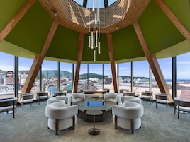 Un salón moderno con una mesa de centro, rodeado de sofás, grandes ventanales que ofrecen vistas a la ciudad y una estructura de techo de madera.