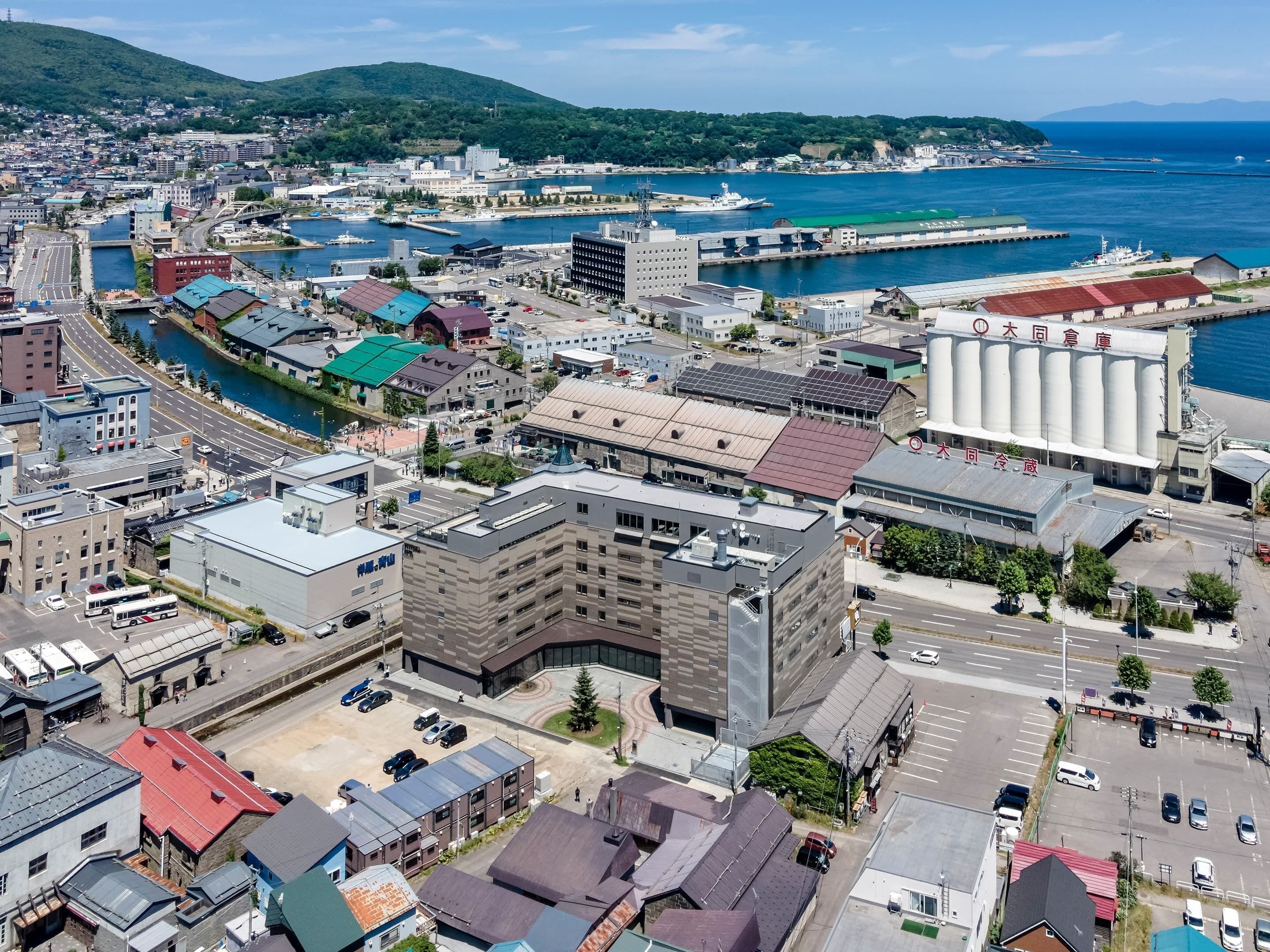 A coastal cityscape with a mix of commercial and residential buildings, a prominent grain silo, and a marina with boats.