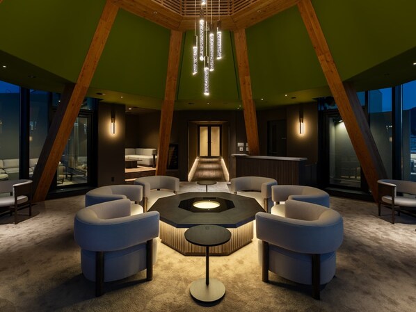 A modern interior with a central seating area, wooden beams, and a view through large windows.
