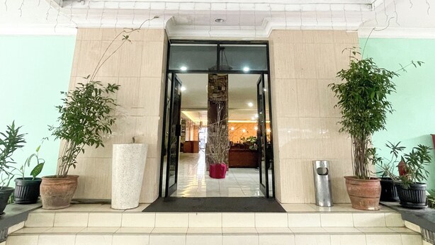 A hotel entrance with a tiled floor, a central doorway, and potted plants on either side. - Hotel Posters (Bandung)