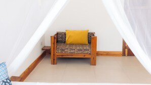 A small, cozy room with a wooden bench and a yellow cushion, a white wall, and a wooden floor. - Olive House - Private Pool, AC & Wi-Fi (Nungwi)