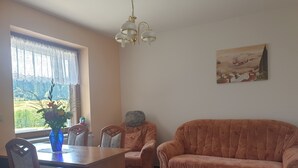 A living room with a dining table, two chairs, a sofa, a chandelier, and a painting on the wall. - Siegmundsburger Haus Werraquelle here Apartment "Traumwelt" family- / pet-friendly (Siegmundsburg)