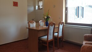 A dining area with a wooden table and chairs, a vase with flowers, a clock, and a window with a view of buildings. - Siegmundsburger Haus Werraquelle here Apartment "Traumwelt" family- / pet-friendly (Siegmundsburg)
