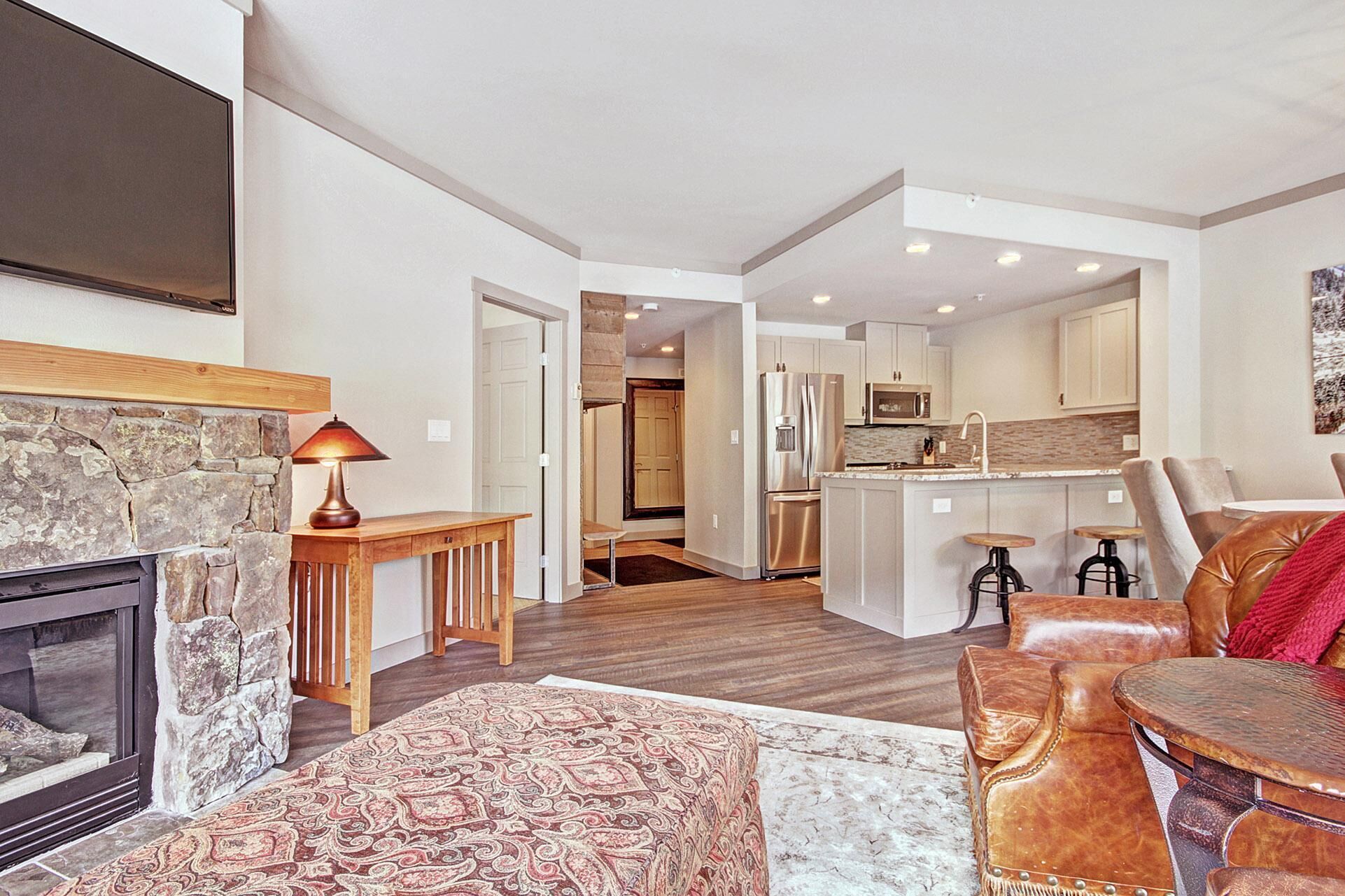 A spacious living room with a fireplace, a cozy seating area, and a kitchen in the background.