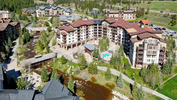 Un hôtel à plusieurs étages doté d’un espace piscine, entouré d’une rivière et de collines boisées.