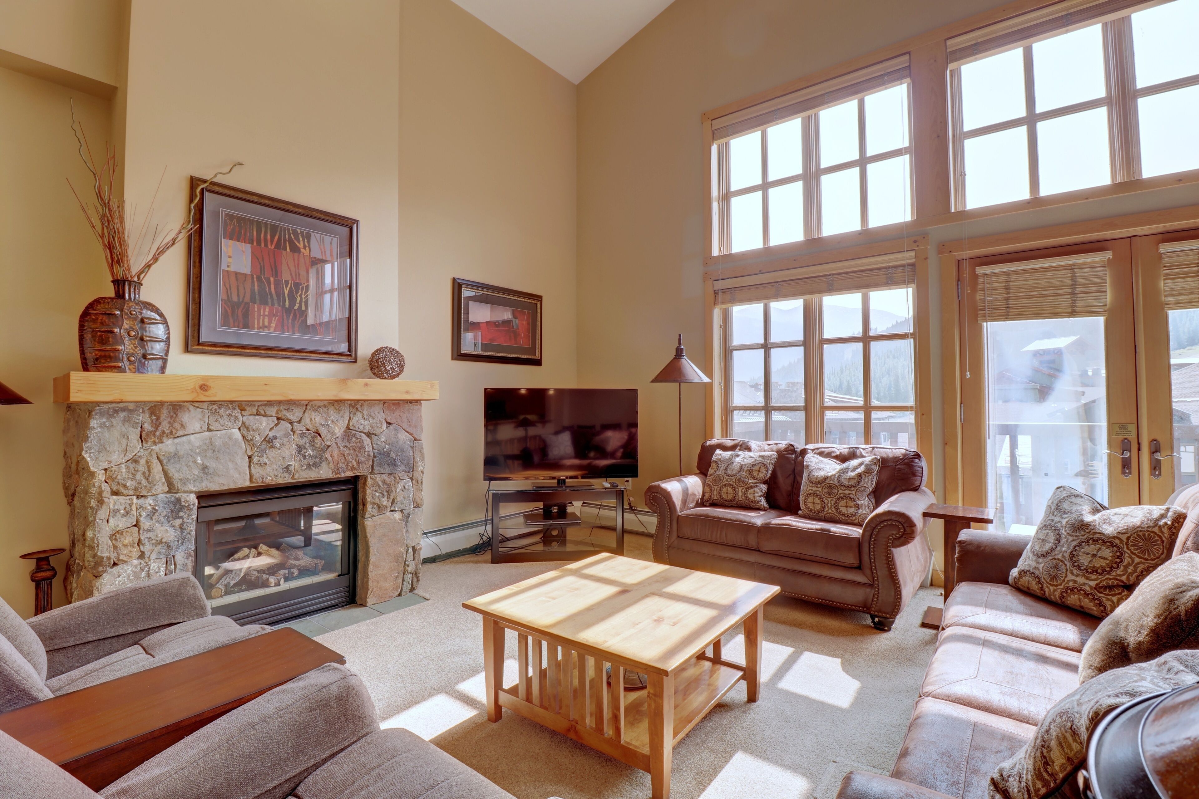 A spacious living room with a stone fireplace, large windows, and comfortable seating.