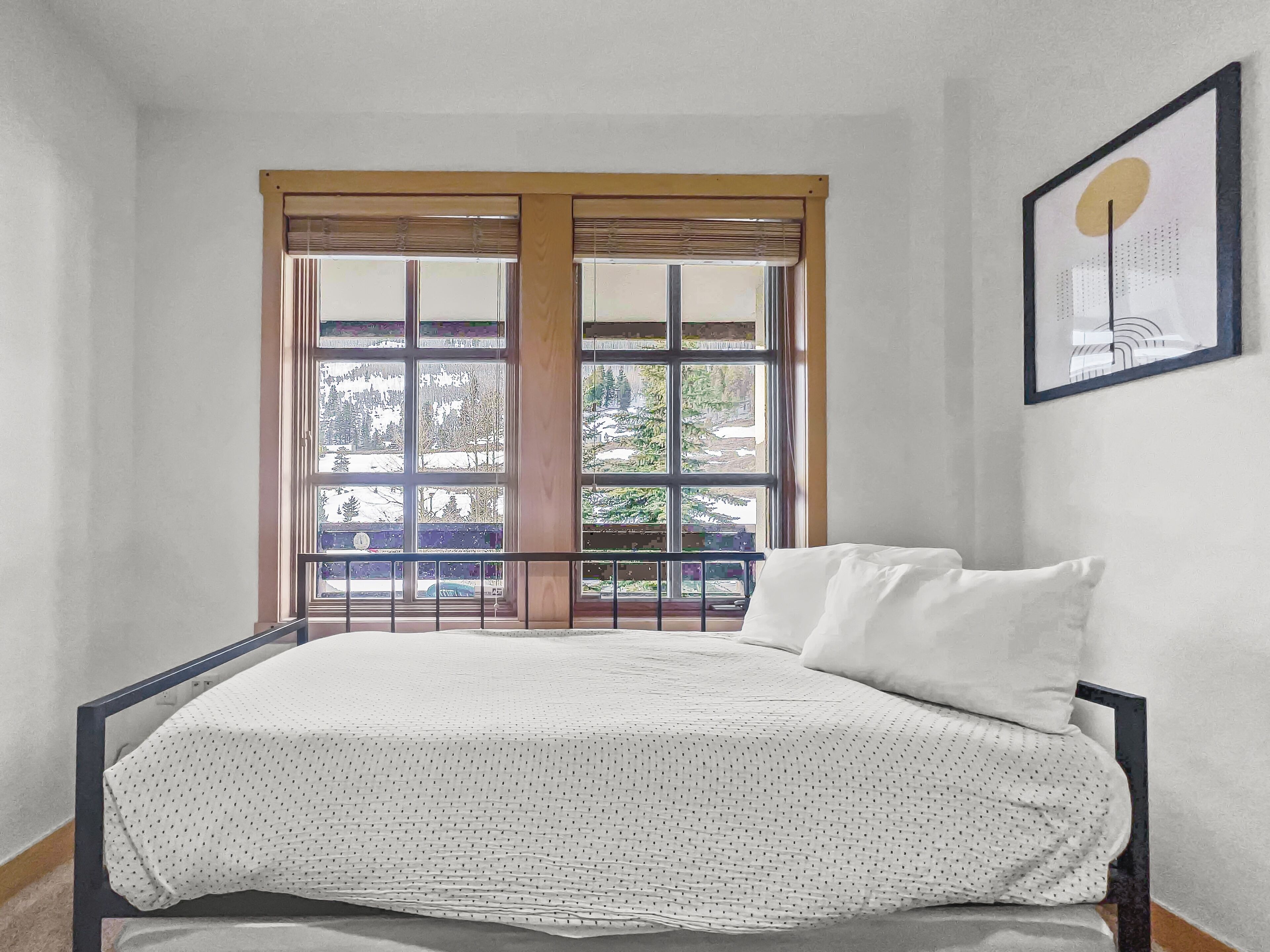 Un dormitorio con cama, ventana con vista a árboles y un coche, y un cuadro en la pared.