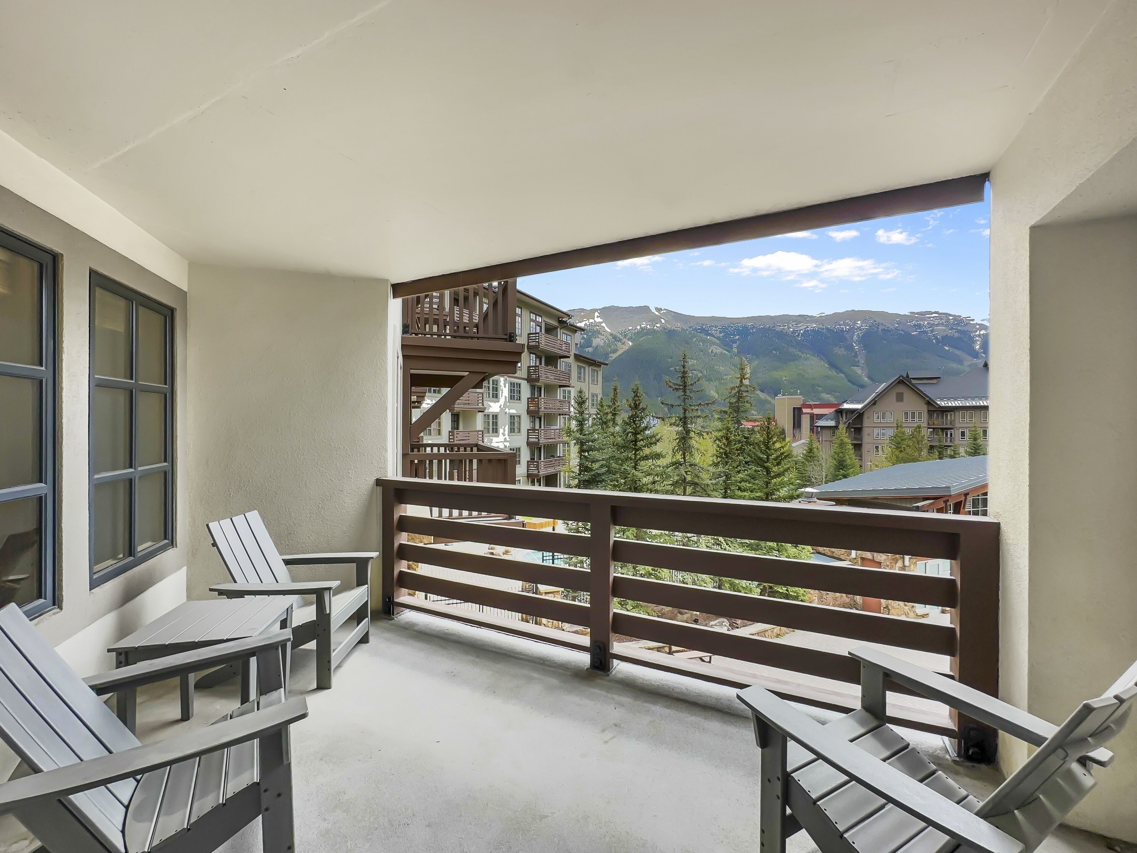A balcony with a view of a mountain range, wooden railings, and a table with chairs.