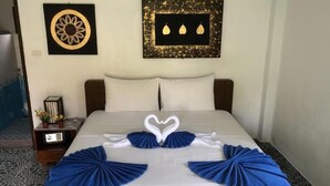 A neatly made bed with a heart-shaped towel arrangement, a nightstand with a clock, and two framed artworks on the wall. - D&K Smiley Phuket Resort (Rawai)
