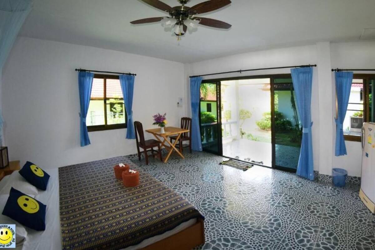 A room with a bed, a small table with chairs, a ceiling fan, and a television.