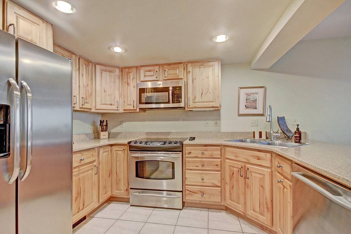 A kitchen with wooden cabinets, stainless steel appliances, and a tiled floor.