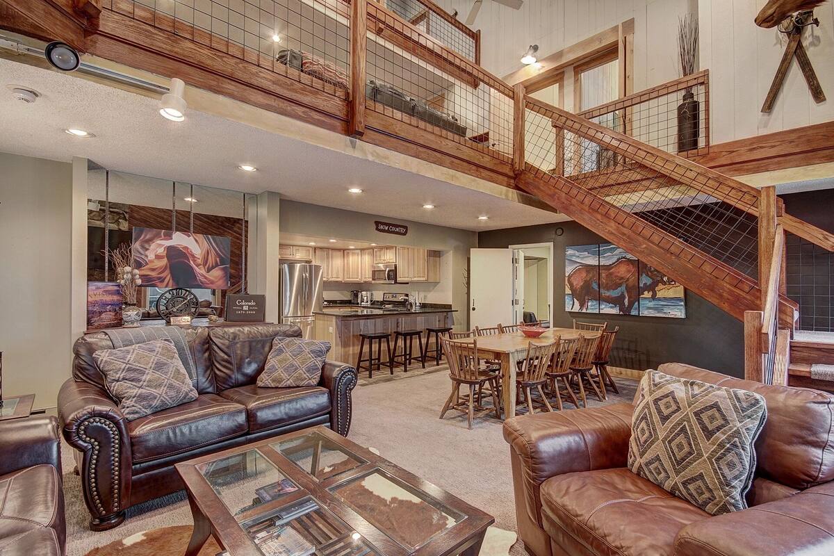A spacious living area with leather sofas, a glass coffee table, and a kitchen in the background.