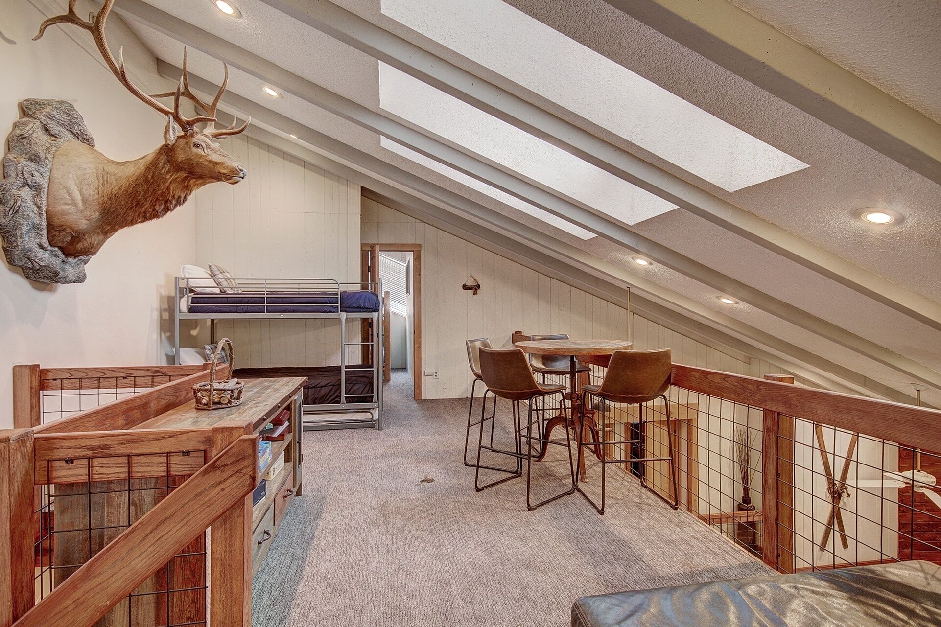 A loft bedroom with bunk beds, a dining area with chairs, and a large deer head mounted on the wall.