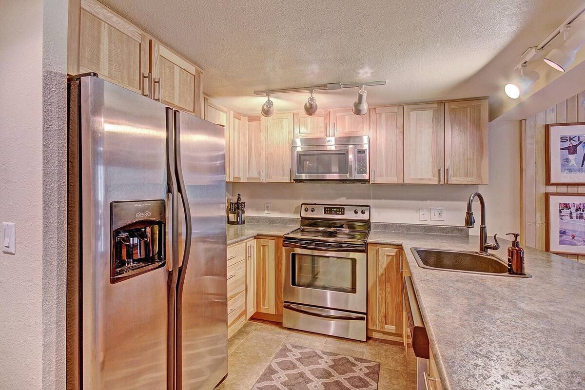 A compact kitchen with stainless steel appliances, wooden cabinets, and a granite countertop.