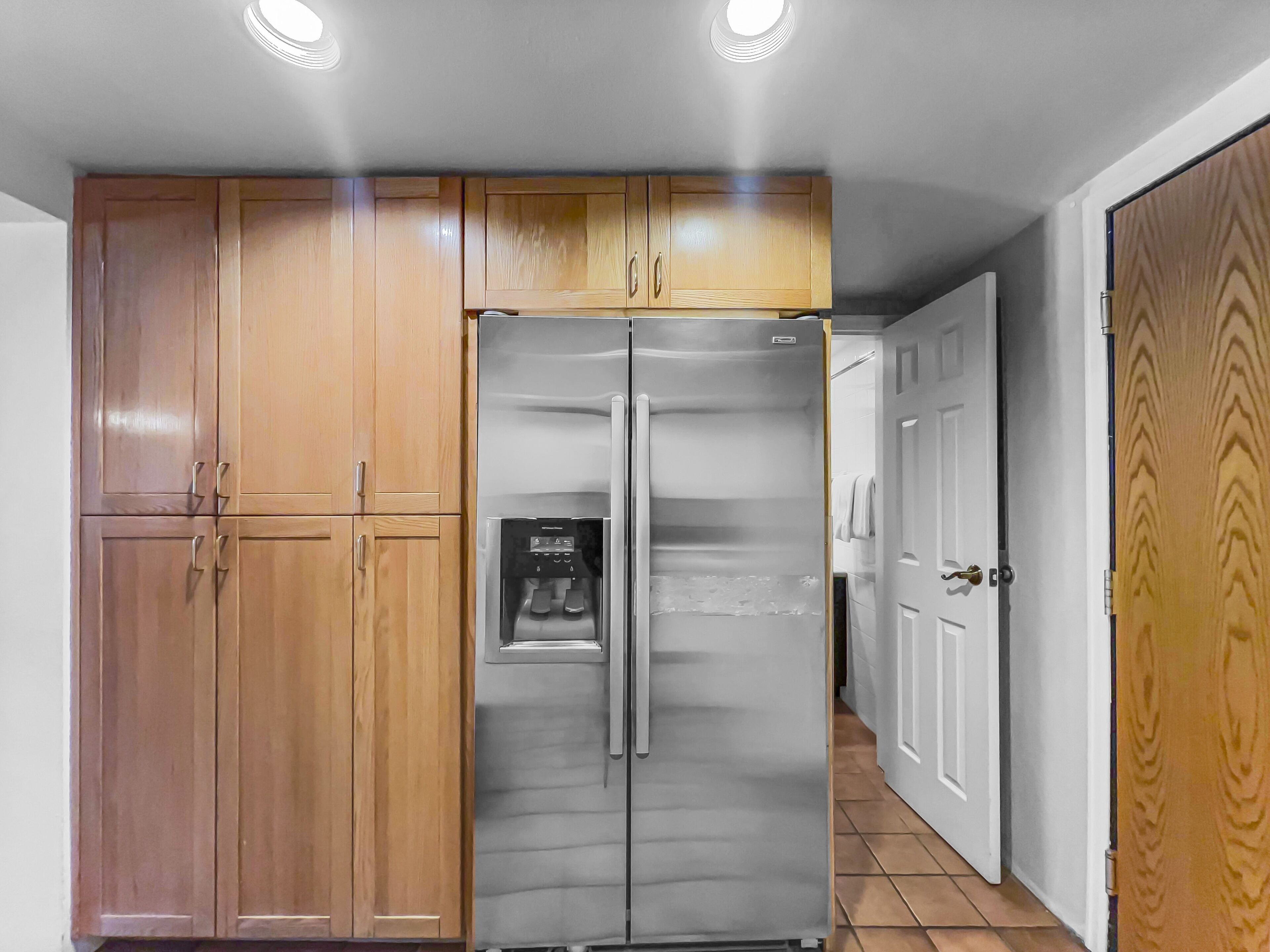 A kitchen with wooden cabinets, a stainless steel refrigerator, and a white door.