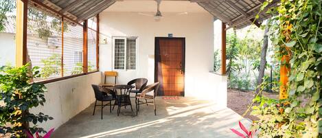 A covered patio with a table and chairs, a wooden door, and a view of the surrounding greenery.