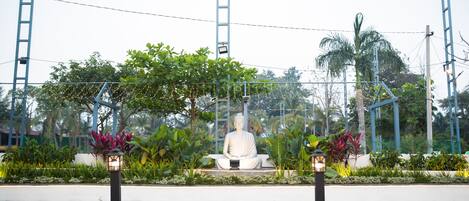 A statue in a garden with a white fence, greenery, and a clear sky.