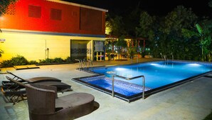 A swimming pool with lounge chairs and a covered seating area, surrounded by a building with a red facade and a tiled deck. - Vanam Resort (Tupran)