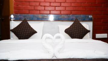 A bed with white linens, a heart-shaped towel arrangement, and a red brick wall in the background.