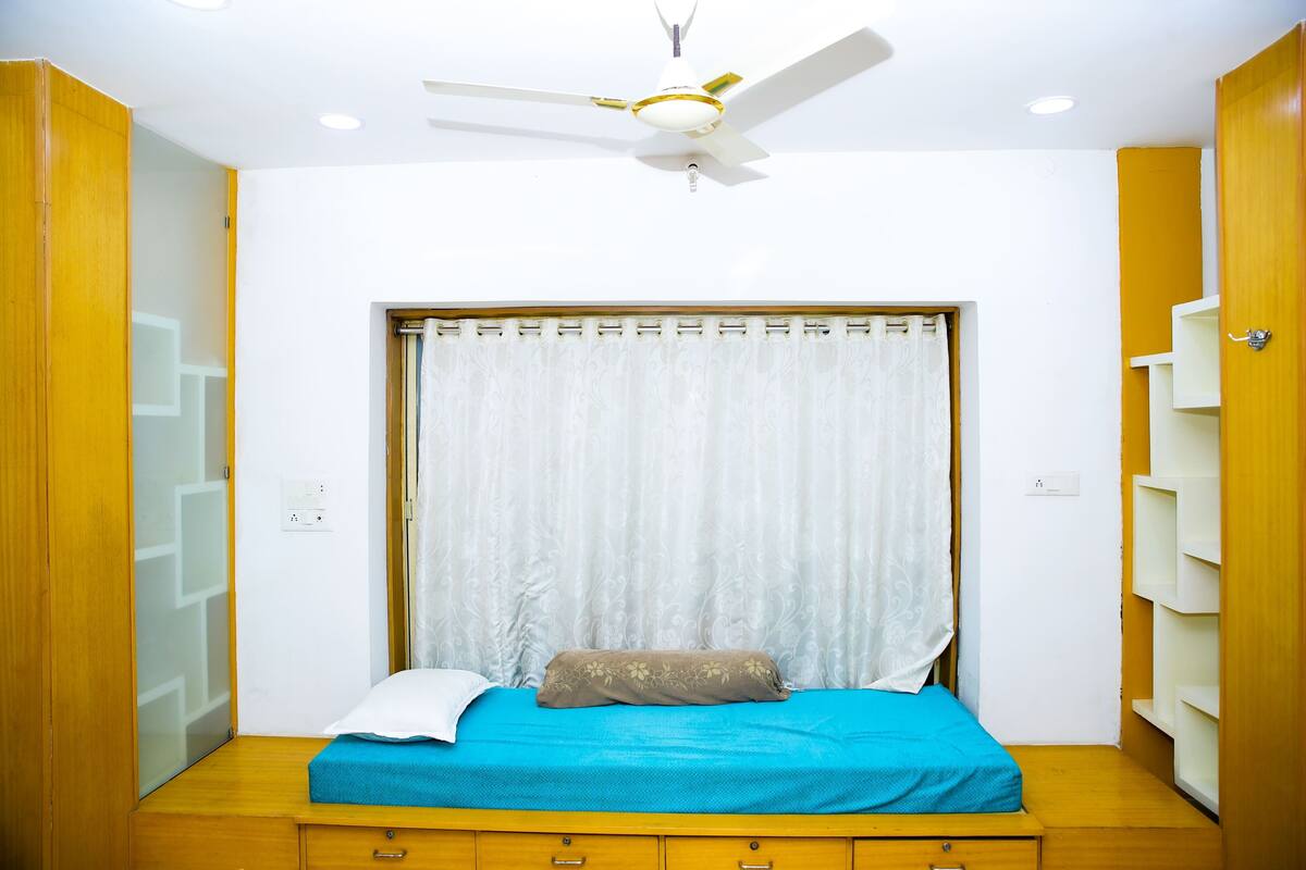 A bedroom with a bed, a ceiling fan, a window with curtains, and wooden furniture.