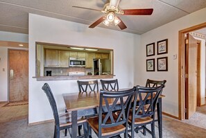 A dining area with a wooden table and chairs, a ceiling fan, a kitchen with a microwave, and framed pictures on the wall. - SkyRun Vacation Homes - Copper Mountain Resort (Copper Mountain)