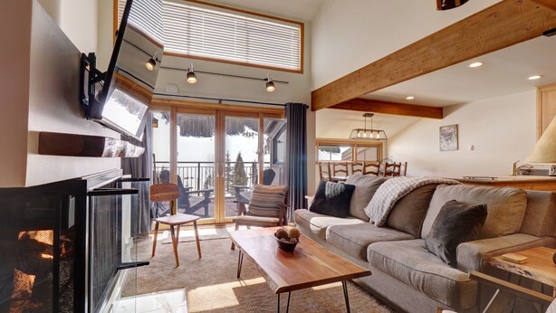 A spacious living room with a fireplace, a sofa, a coffee table, and a balcony with a view of the mountains. - SkyRun Vacation Condos Copper Mountain Resort (Copper Mountain)