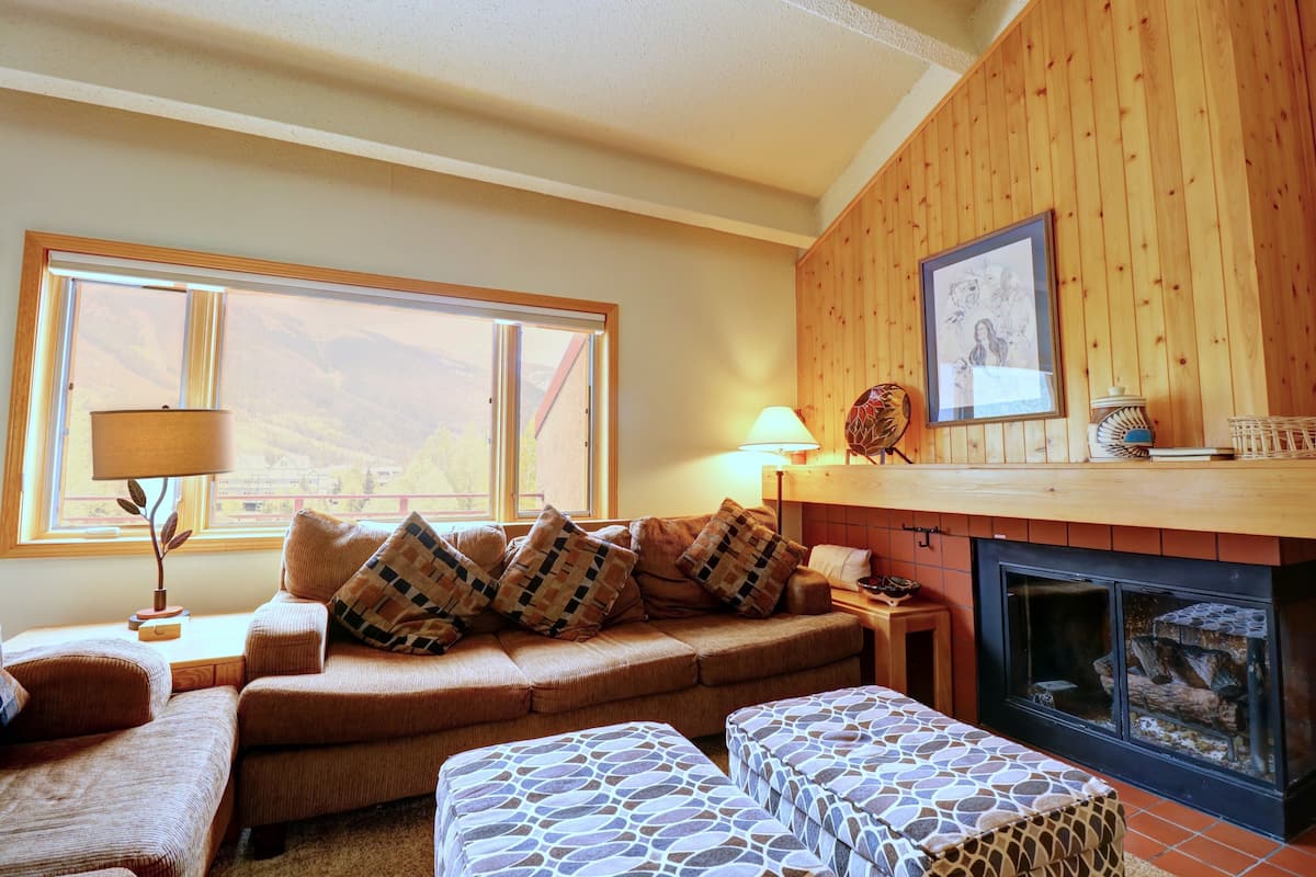 Una sala de estar acogedora con un sofá, un reposapiés y una chimenea.