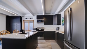 A modern kitchen with a central island, black cabinetry, stainless steel appliances, and a wooden floor. - SkyRun - Copper Mountain Resort Vacation Condos (Copper Mountain)