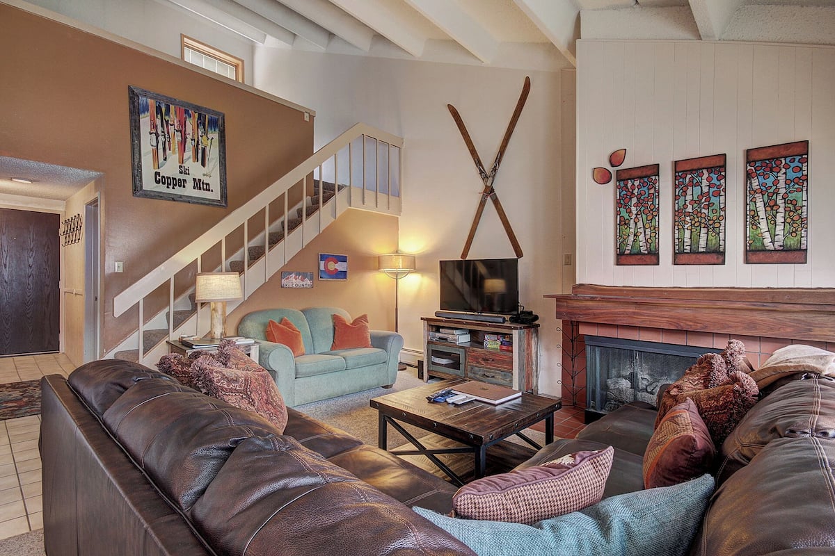 Una sala de estar acogedora con chimenea, televisión y una escalera que conduce a un nivel superior.