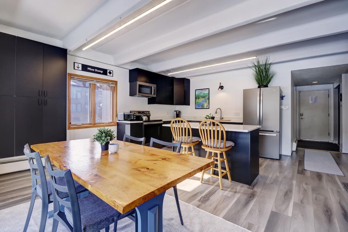 Una cocina moderna con una mesa de comedor de madera, armarios negros y un refrigerador de acero inoxidable.
