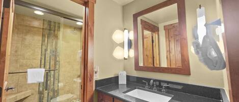 A bathroom with a glass-enclosed shower, a sink with a black countertop, and a mirror with lights.