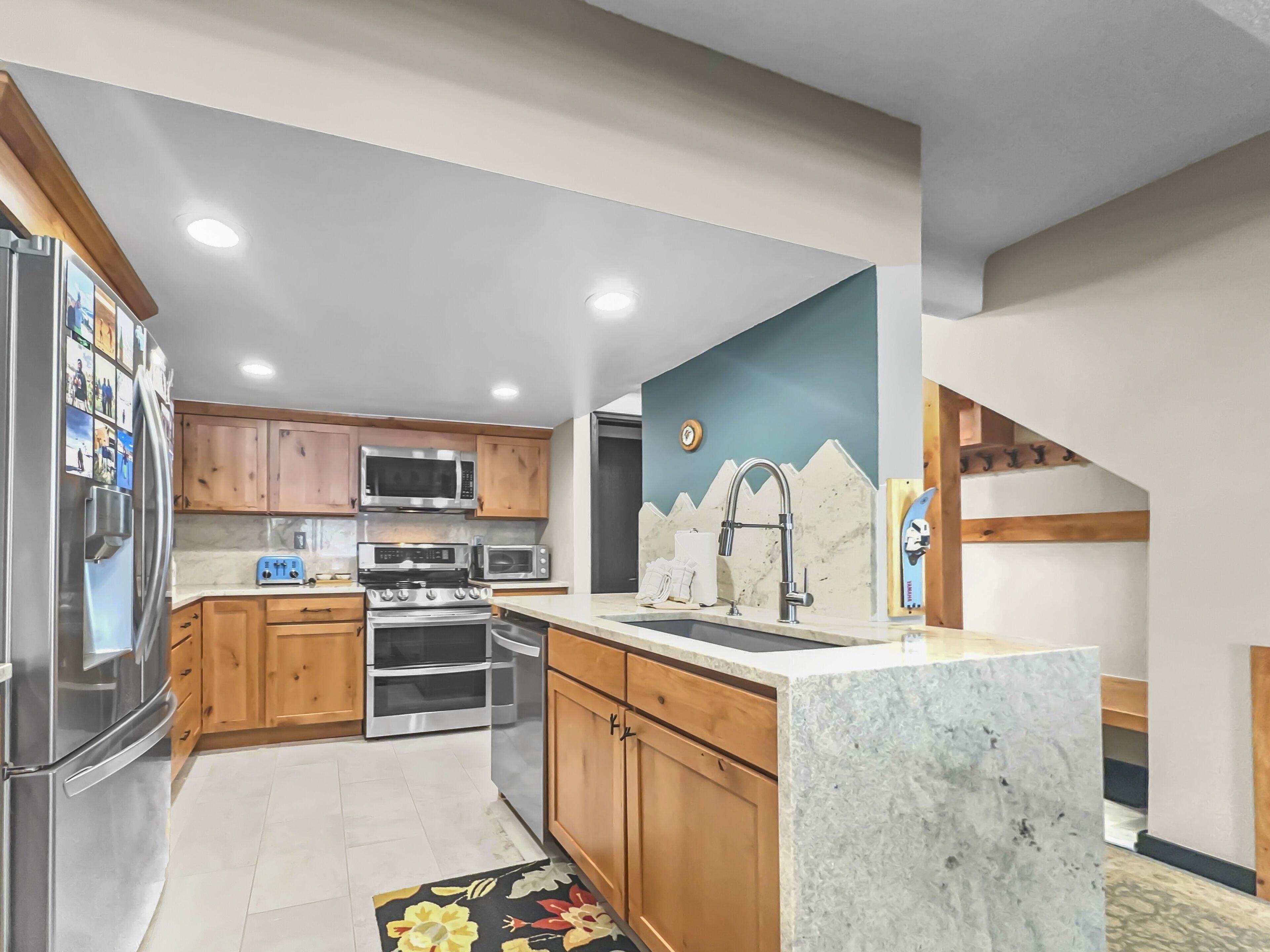 A modern kitchen with wooden cabinets, stainless steel appliances, a marble countertop, and a decorative wall mural.