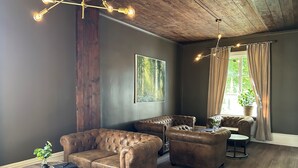 Une pièce avec des canapés en cuir, une table ronde en bois et une grande fenêtre avec des rideaux.