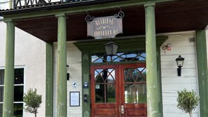 L’entrée d’un hôtel touristique, avec une porte en bois, des colonnes vertes et un balcon orné d’une enseigne.