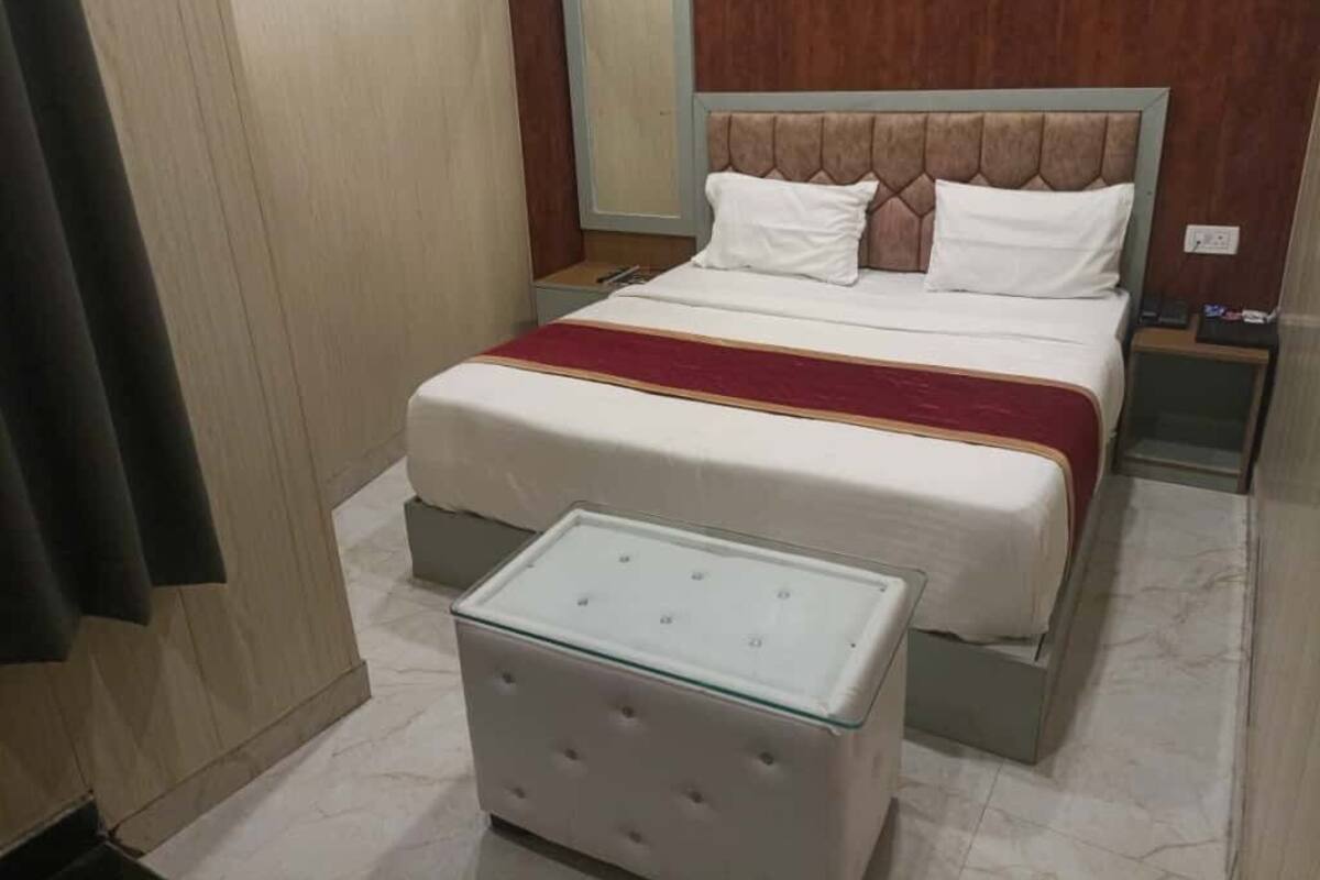 Una cama bien hecha con una colcha roja, una mesita de noche con superficie de cristal y un cabecero de madera.