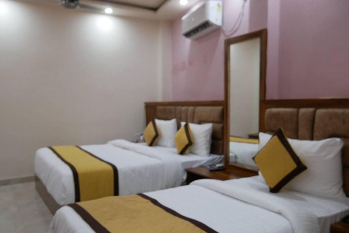 Habitación de hotel con dos camas, cada una con cabecero y almohadas, una mesita de noche y un espejo en la pared.